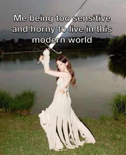 Woman standing by a lake. She has brown hair and wears a white long dress with white trousers underneath. Above her head she brandishes a huge sword. Text reads: Me being too sensitive and horny to live in this modern world.