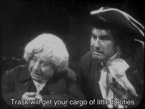Patrick Troughton missing episode reconstruction. Trask and Perkins, a sailor with a tricorn hat and his clerk wearing a white wig, are speaking to someone off-screen in a room that’s too dark to see any scenery or use any budget. Caption reads, “Trask will get your cargo of little booties”