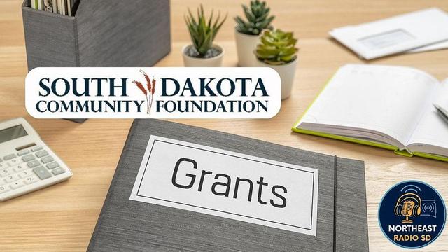 Office desk with a binder labeled "Grants," plants, calculator, and notebooks. Logo for South Dakota Community Foundation and Northeast Radio SD.