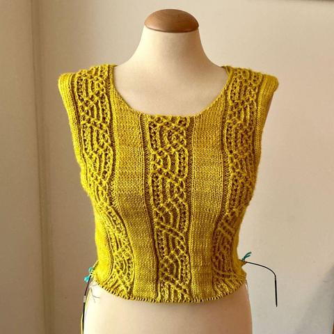A sweater knitting project on a circular needle and shown from the front on a mannequin against a white background. The yarn is bright yellow.