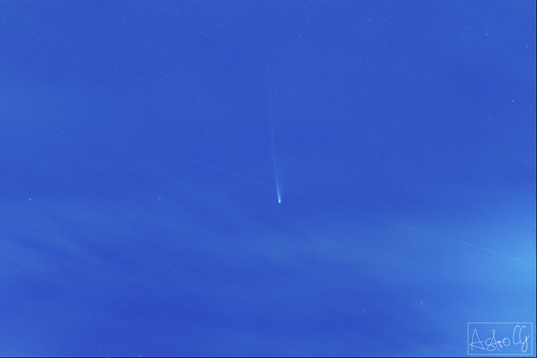 Comet in the center of the image in a blue starry star. Faint clouds surrounding it.