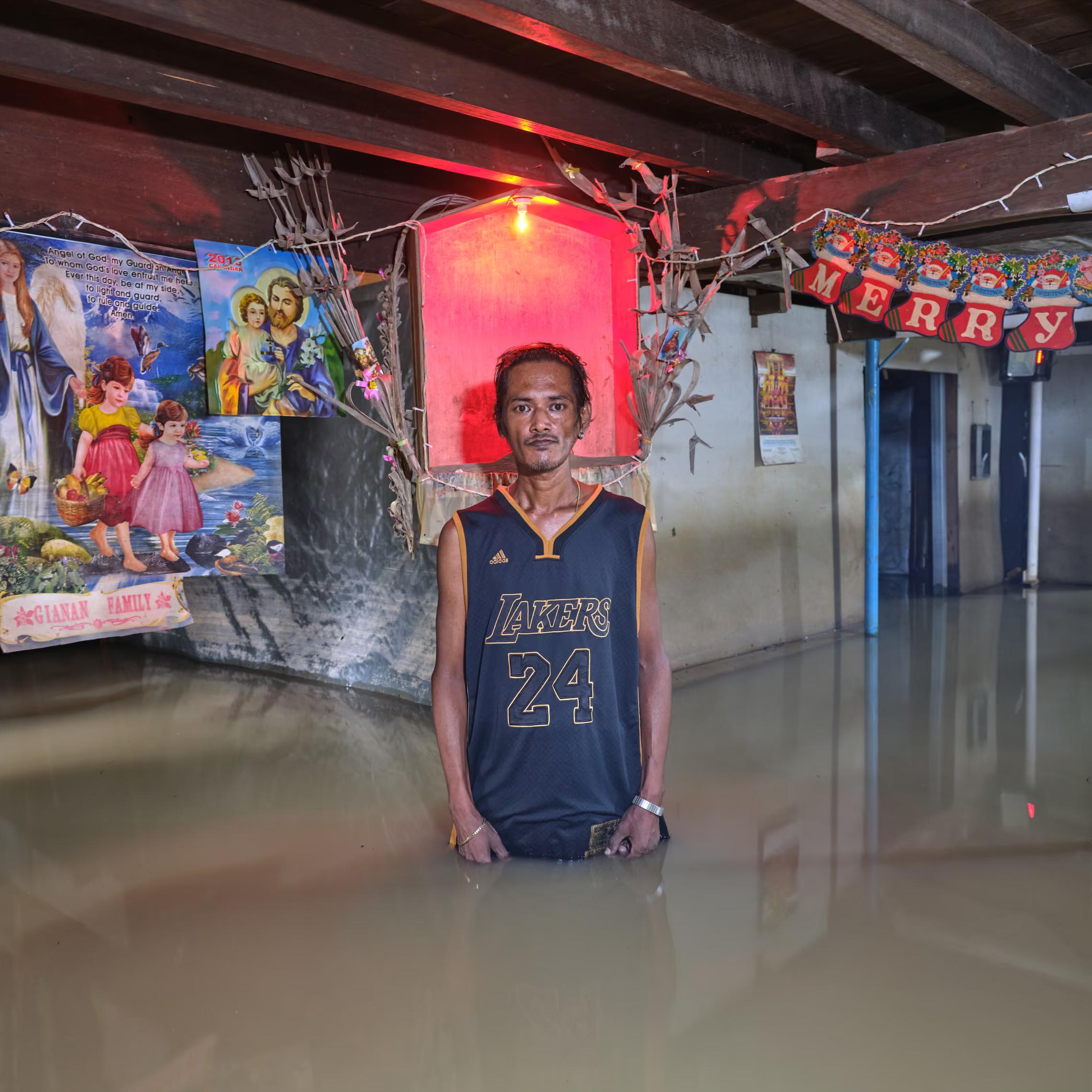 A man stands in water inside his flooded house, with holy pictures and a Merry Christmas banner on the walls.
"We have had water here since Typhoon Emong in July. We know now what is going on because it’s in the news – many have become corrupt, and the funds for flood control construction have disappeared."