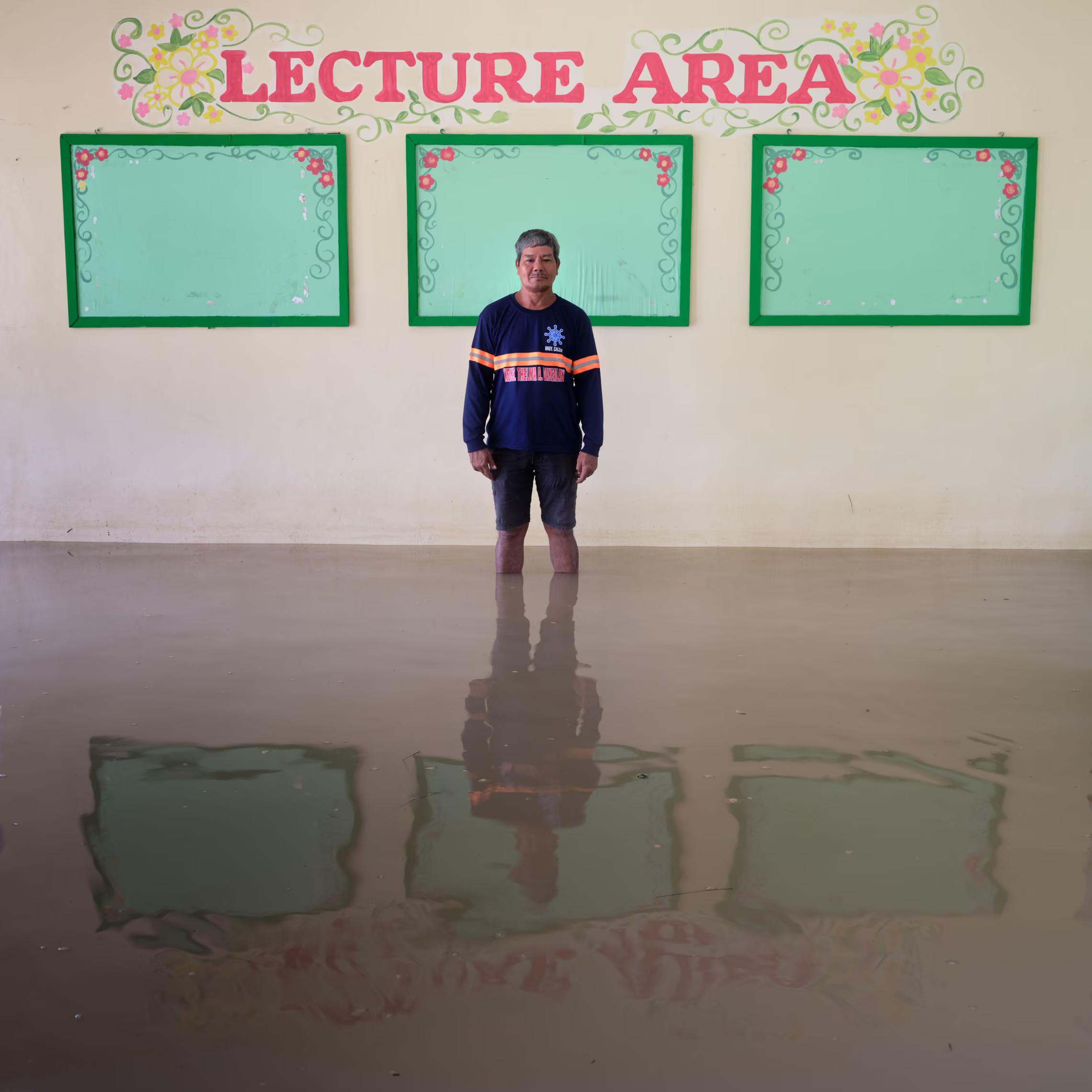 A man standing in a flooded classroom in front of three green whiteboards.
"Every year now there are at least two typhoons and they are getting more frequent. Our community is near a river and close to the sea so the floodwater from the whole country eventually reaches us, and the high tide makes it much worse."