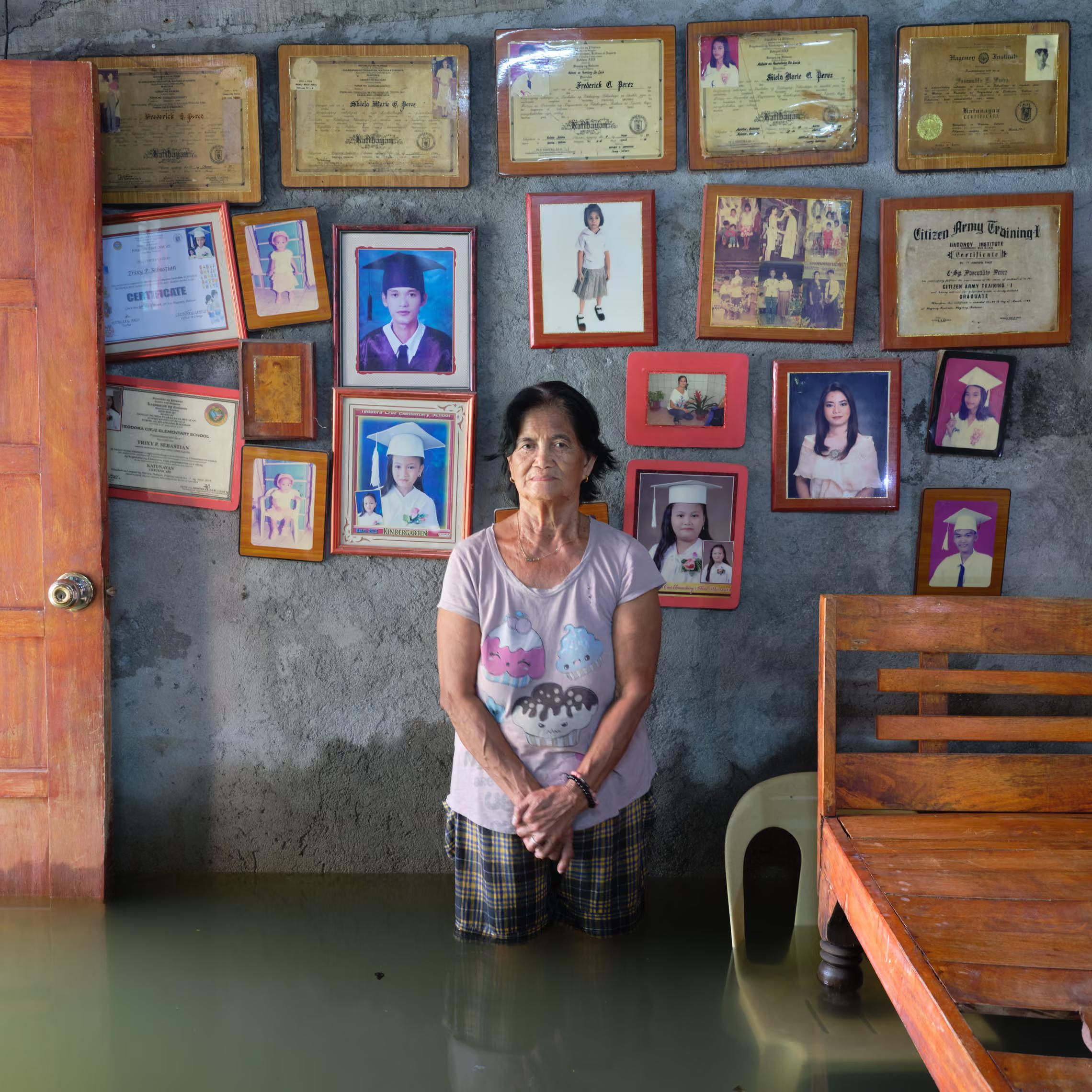 A 76-year-old woman stands inside her flooded house, with pictures of her children on the wall behind her.
"The only time we saw water before was if we went to the river. My message to the world is for this water to stop entering the houses and the streets. We end up with nowhere to sleep, nowhere to move our things."
