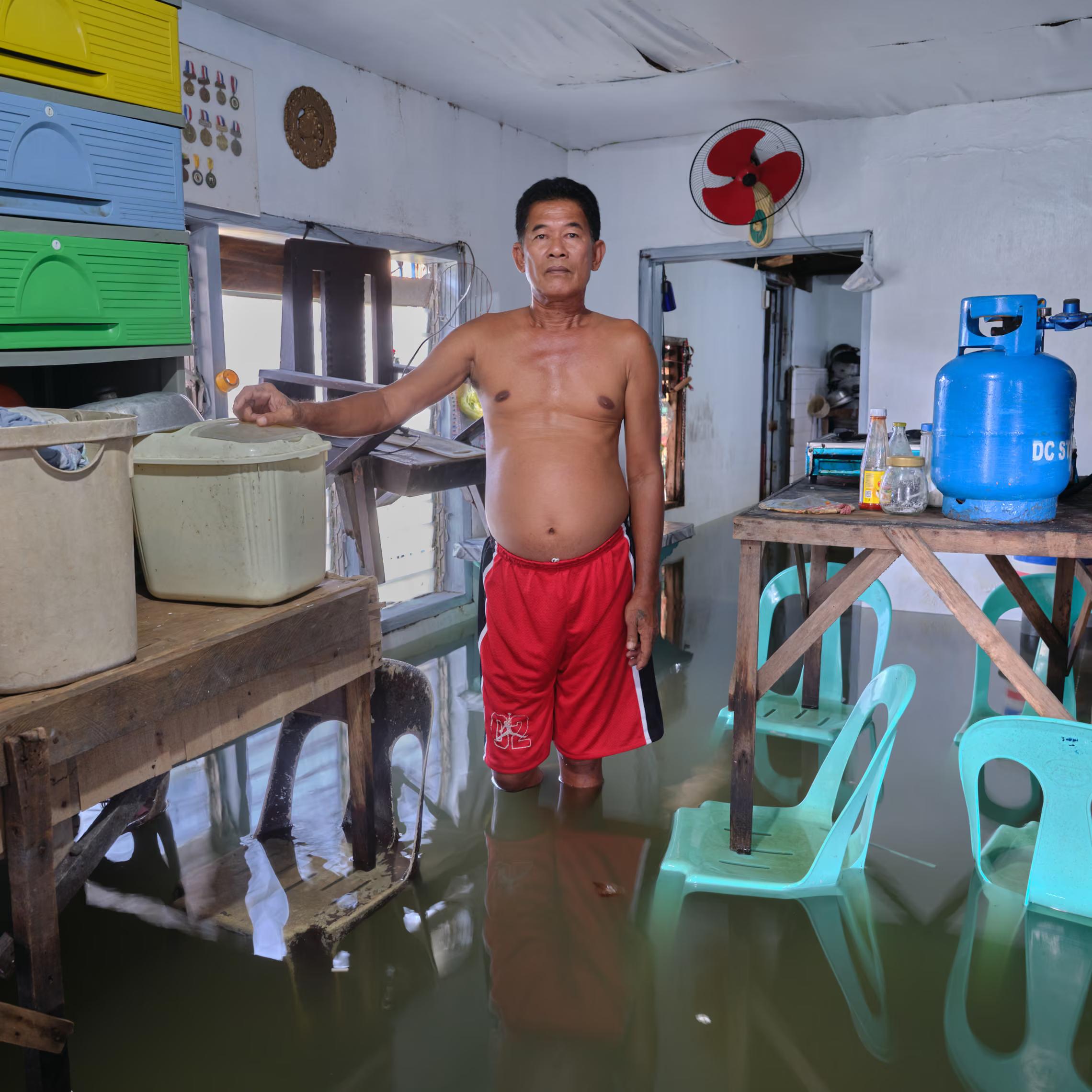 A man in red shorts stands in his flooded kitchen.
"Secondly there is corruption. That won’t be eliminated. Before, there were many trees here. You wouldn’t be affected by high tide. Now, the trees are slowly disappearing. The careless disposal of trash is also a big reason."