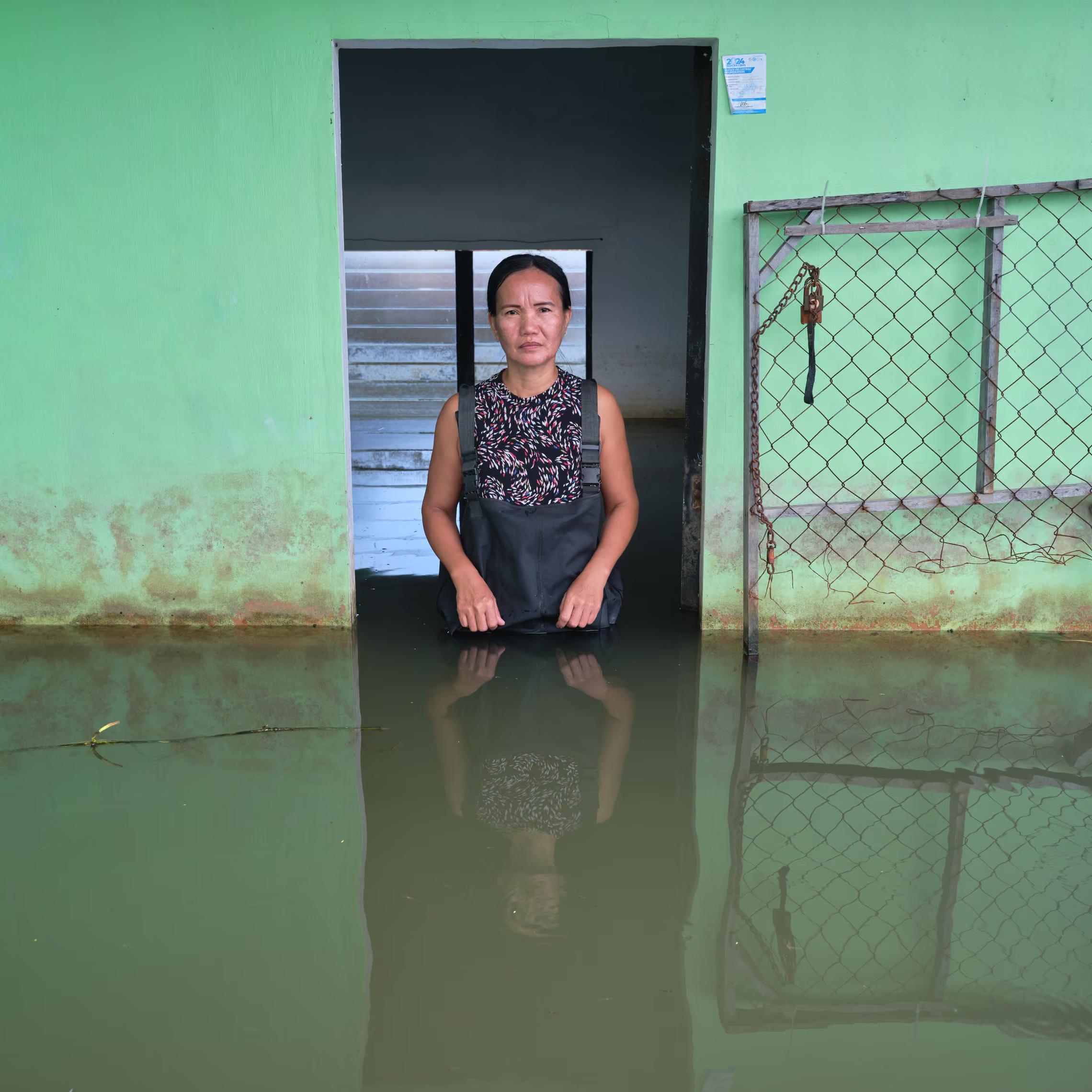 A woman stands in the doorway of her flooded house.
"It seems like the storm is getting stronger and stronger all the time. The wind is strong. The rain is strong. It seems like it doesn’t stop. To all the leaders, you must help us, take action on this flood."