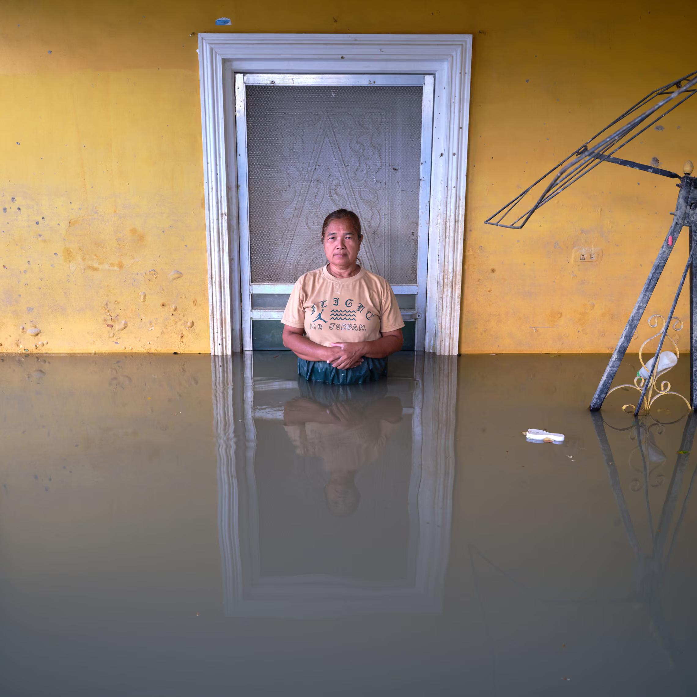 A woman stands in her flooded house, waist-deep.
"Because when it rains in our area, we get flooded. Now it’s not raining, we still get flooded. It seems like there’s no sun anymore, only rainy season."