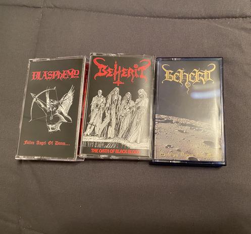 Three bestial black metal cassettes. From left to right: "Fallen Angel of Doom" by Blasphemy, "The Oath of Black Blood" by Beherit, and "Drawing Down the Moon" also by Beherit.