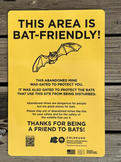 Black text on bright yellow metal sign with a line art drawing of a cute bat on it that reads in part:
THIS AREA IS
BAT-FRIENDLY!
THIS ABANDONED MINE
WAS GATED TO PROTECT YOU.
IT WAS ALSO GATED TO PROTECT THE BATS
THAT USE THIS SITE FROM BEING DISTURBED.
Abandoned mines are dangerous for people
but are great places for bats.
Please stay out of abandoned mines like this
for your safety and for the safety of
the wildlife that use it.
THANKS FOR BEING
A FRIEND TO BATS!
LEARN MORE:
COLORADO
Division of Reclamation,
Mining and Safety
Department of Natural Resources
THIS SIGN WAS
SUSTAINABLY DESIGNED
AND MADE IN COLORADO.