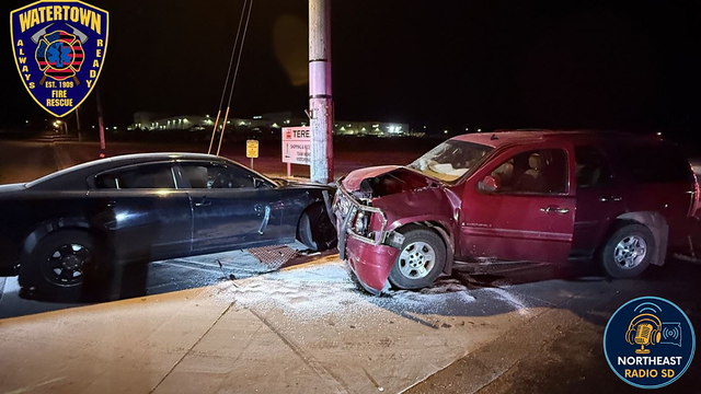 Two cars, one black and one red, collided head-on at night near a streetlight. Watertown Fire Rescue and Northeast Radio SD logos visible.