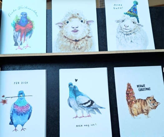 Sechs Postkarten mit Aquarellmotiven: Tauben, Schafe und eine Katze, teilweise mit Weihnachtsdeko, teils mit kurzen Texten wie 'FÜR DICH' und 'DICH mag ich!'.