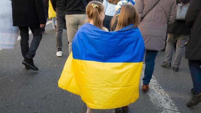Deux jeunes enfants marchent ensemble avec un drapeau ukrainien sur les epaules, lors d'une manifestation de solidarité avec le peuple ukrainien le 23 fevrier 2025 à Paris.