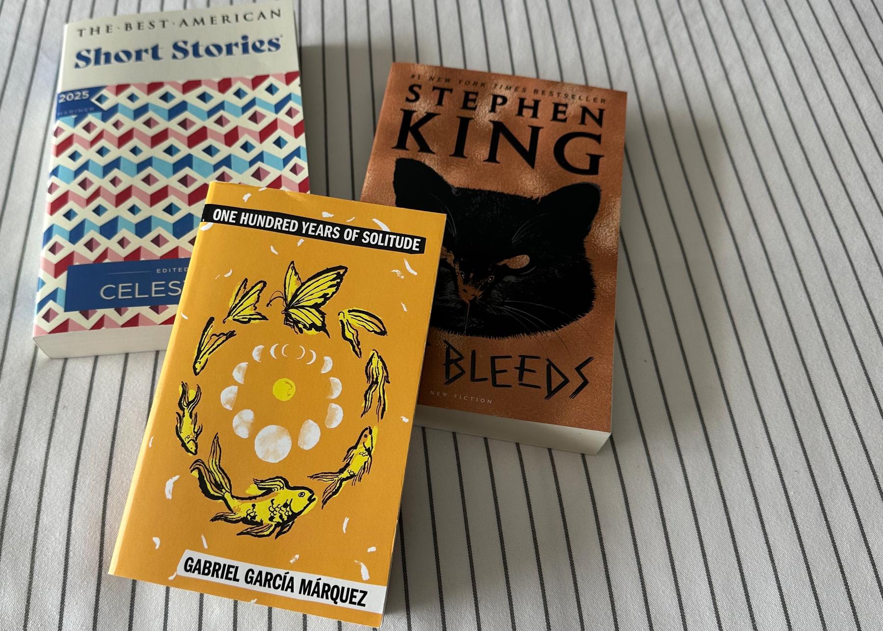 Three books on a bed: The Best American Short Stories, One Hundred Years of Solitude, If It Bleeds. 