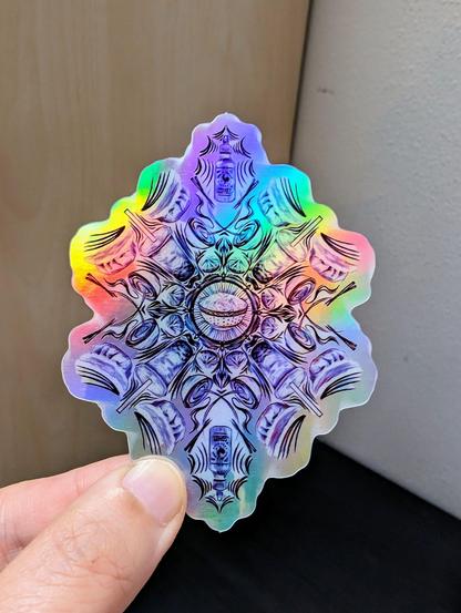 Photo of a left hand holding a diecut sticker. The sticker is a holographic drawing of an Asian food themed mandala.