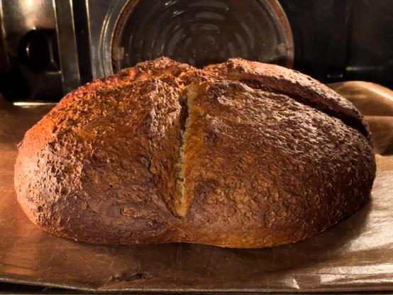 Blick in geöffneten Backofen. Auf Backfolie liegt ein Laib Brot.