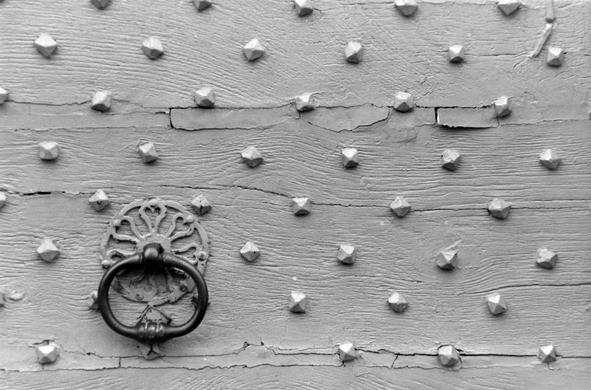 Un porte en bois avec de gros clous et un heurtoir en forme de poing