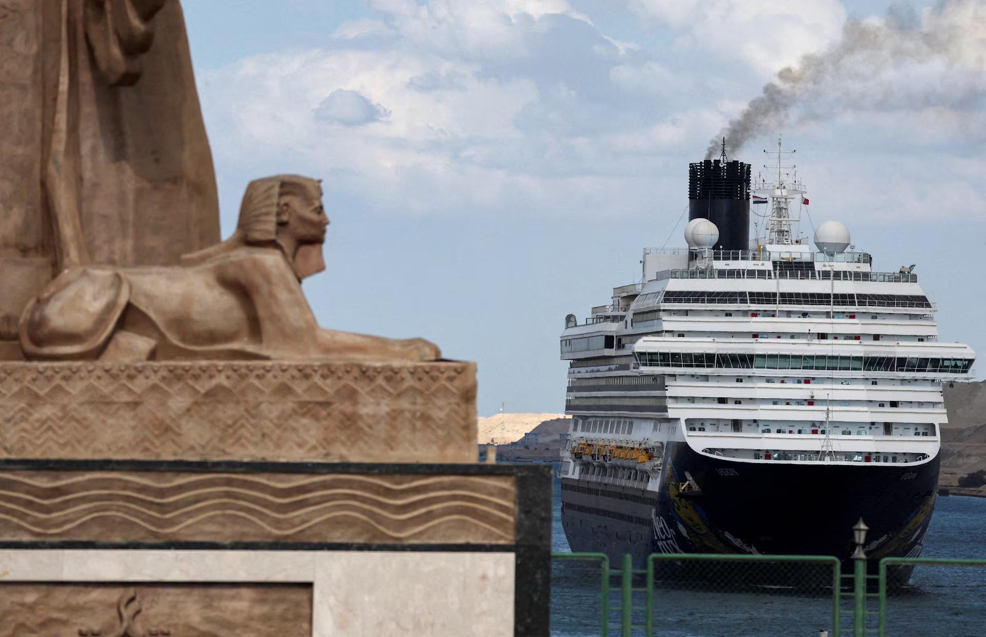 A cruise ship passes through the Suez Canal, watched by a sphinx.