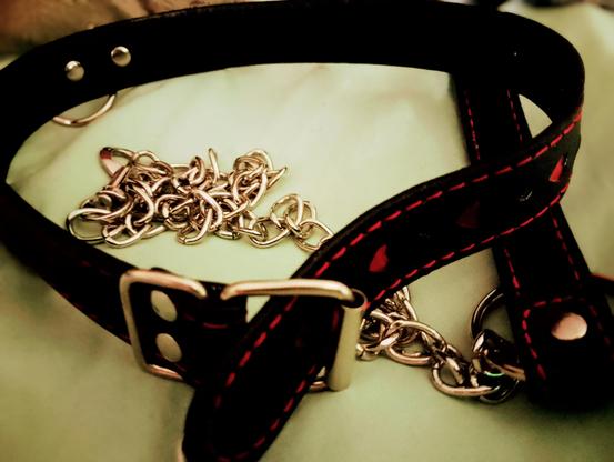 Black bdsm collar with red hearts and sticking, and a matching leash with red stitching on the handle.