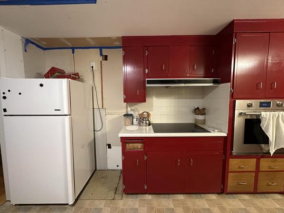 Elevation view of the West wall of our kitchen. The cabinets are red painted MDF over old laminate. One small cabinet has been removed and the flooring beneath it and the fridge has also been removed. The fridge was returned to the corner and the removed cabinet has not been put back in place. 
