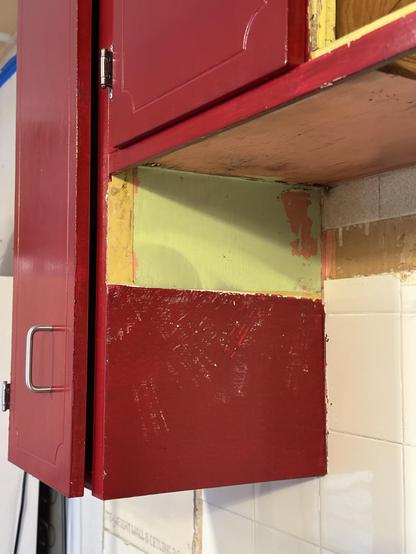 A red upper cabinet in our kitchen. The side that was covered by a vent shows layers of yello, green, and pink paint. 
