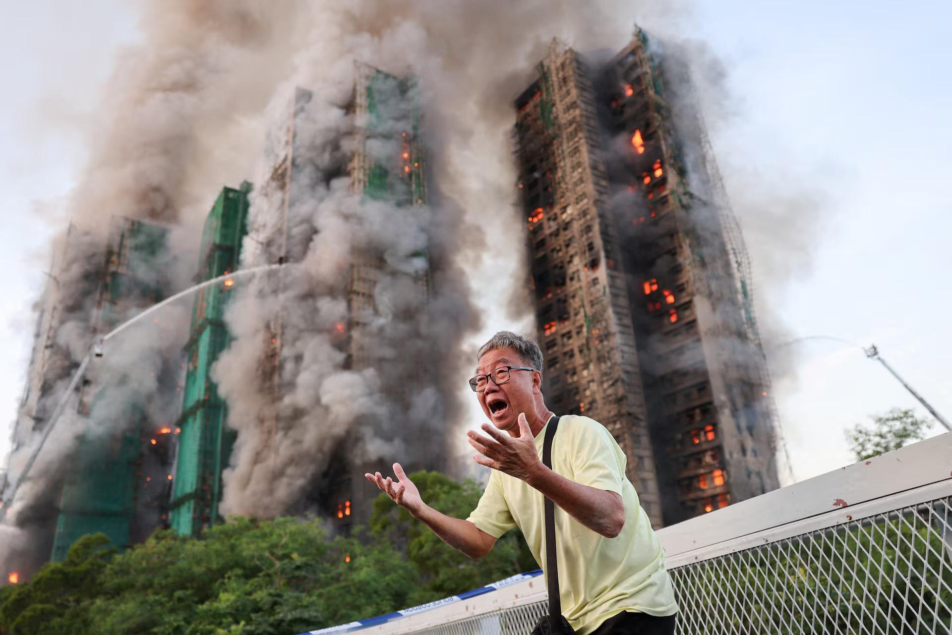 A man in despair in front of eight high rise apartment buildings engulfed in fire.
Tyrone Siu