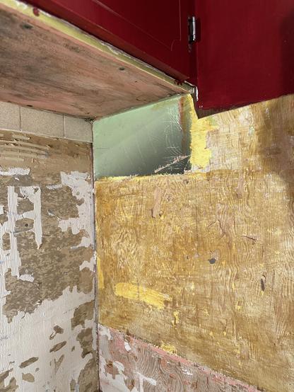 Closeup of the corner where the wall oven cabinet meets the West wall. A small rectangle of lime green paint, previously hidden by the vent/hood, shows darkening along the lower front corner, indicating that burning or scorching from the cooktop  happened at some point. 