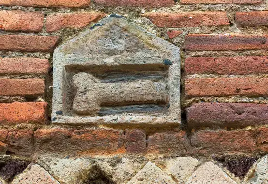 A red brick wall with a small decoration of an erect phallus inside a building in white stone.