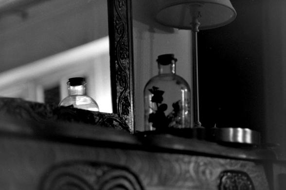 Une bouteille et son reflet dans un miroir, sur une cheminée, en noir et blanc