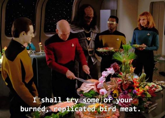 Star Trek The Next Generation scene. The Enterprise D gang is in Ten Forward standing around a beautifully decorated banquet table adorned with exotic flowers and lots of food. Seems like a fancy party is happening, I'm guessing some light chitter chatter is in the background, dishes and flatware tinkling and clanking, maybe some nice soft harpy music, but this is a picture so it's tough to say. Ok, back to the story, so Captain Picard is carving a large round turkey. Bev Crusher, Geordi, Data, and a very very tall Klingon, all in uniform, stand and observe. Closed caption reads, "I shall try some of your burned, replicated bird meat." 🦃