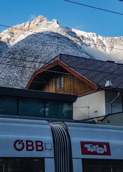 A sunlit mountain top above a railway station with a train in the foreground. 