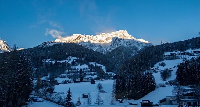 High mountains peaks covered in snow in sunlight, with a valley below full of snow and in shadow.