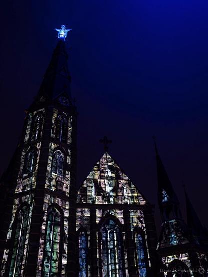 Blue night with church covered with projected faces, on the top a Christ statue.  