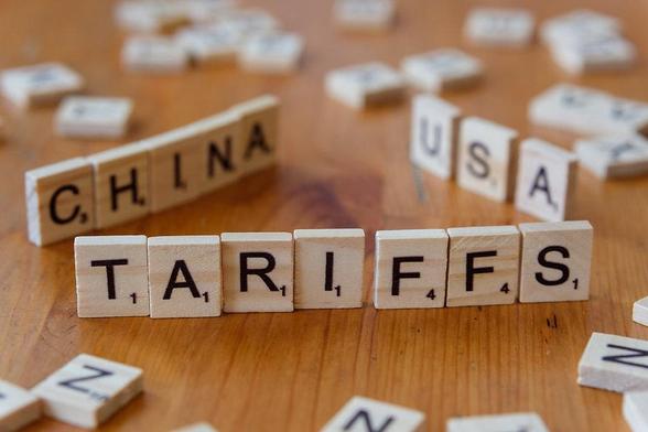 Scrabble tiles spell "TARIFFS" with "CHINA" and "USA" in the background on a wooden surface, suggesting trade themes.