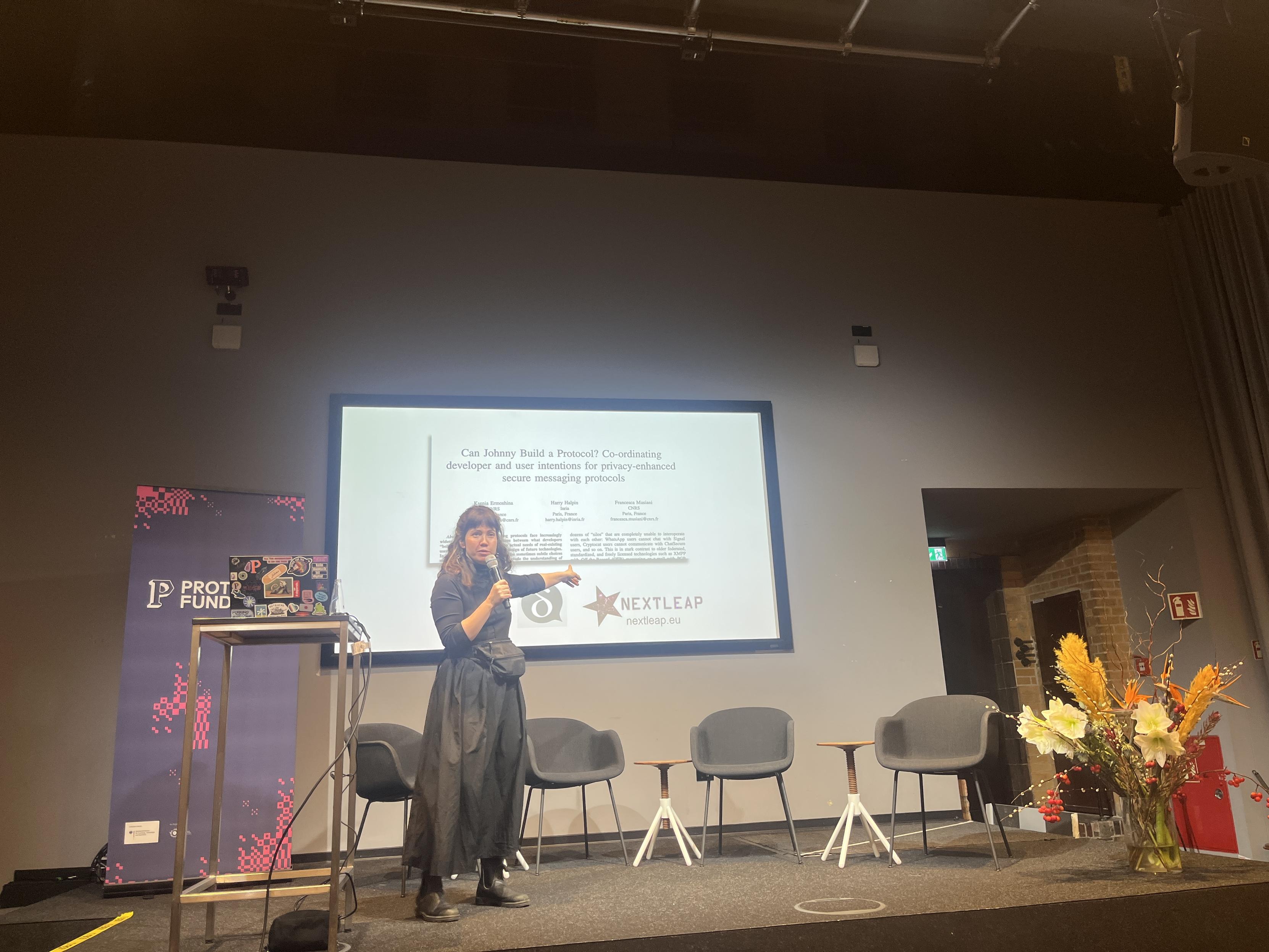 Foto einer Person, die auf der Bühne steht und auf die Folien hinter ihr zeigt