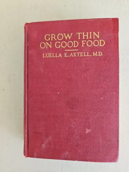 Cover image of the book Grow Thin on Good Food by Luella E. Axtell, M.D.

he book cover shown is a plain, deep red hardback with a textured surface. Centered near the top, the title “GROW THIN ON GOOD FOOD” is printed in bold, gold uppercase lettering. Beneath it, also in gold, is the author’s name: “LUELLA E. AXTELL, M.D.”