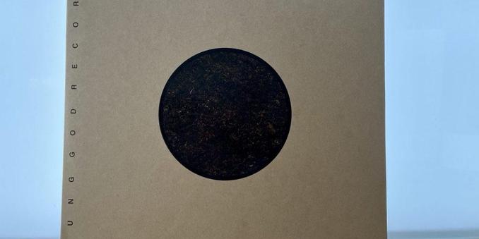 Ein brauner Kartoneinband mit einem großen schwarzen kreisförmigen Motiv auf der Vorderseite und dem vertikal an der Seite aufgedruckten Text „UNG GOD RECORDS”.
