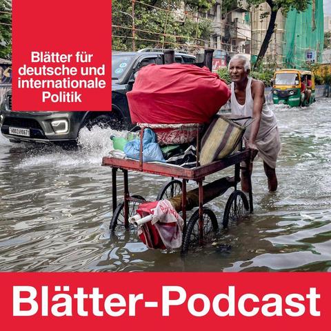 Ein Mann schiebt einen Karren durch eine Überschwemmung. Im Hintergrund fährt ein SUV. (IMAGO / NurPhoto)