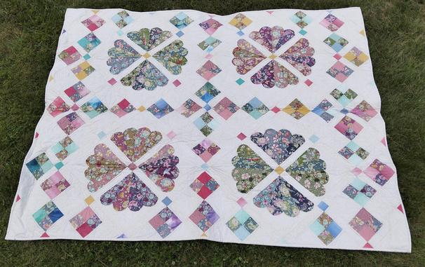 a quilt, it if 4 plate-like designs in differing colorful fabrics, the quadrants separated by strips of triangles, lots of blues and pinks and some gold, against a white background 