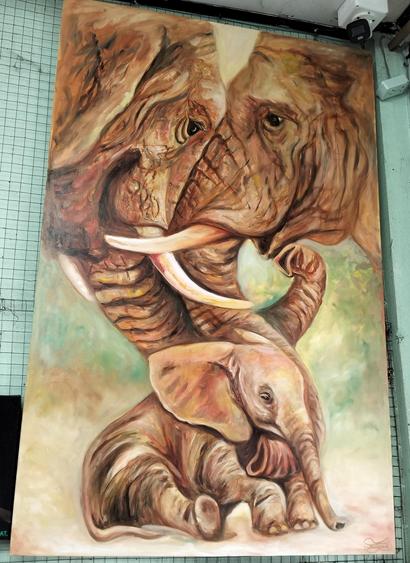 a young elephant , sitting on a dusty ground, two adults leaning in and caressing it with their trunks, blurred green and tan background 