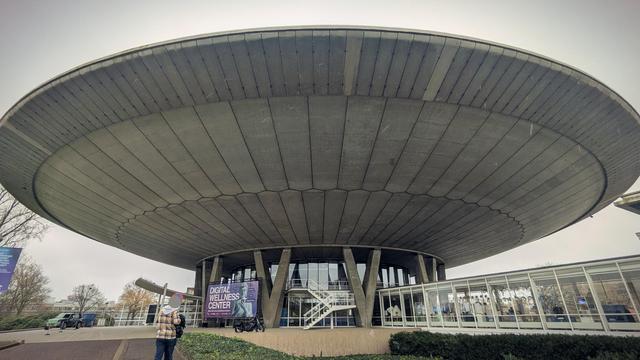 A building in the shape of a flying saucer made of concrete, perched on a center pillar made of concrete and glass.