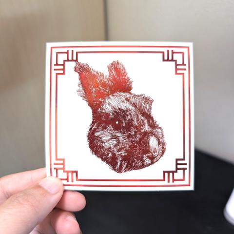 Photo of a left hand holding a square sticker. The sticker is a holographic drawing of the Chinese Zodiac animal: the Rabbit.