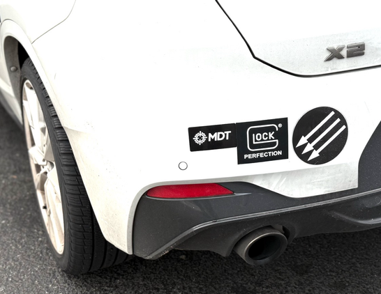 Photo of the rear of a car with bumper stickers. The first is a sticker that’s says “MDT”. The second is a Glock sticker. The third is an Italian anti-fascist symbol.