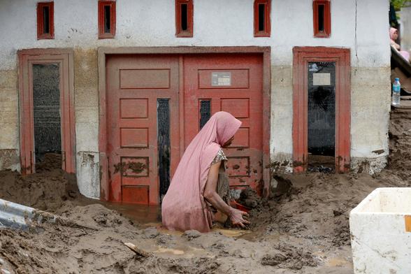 A woman clears mud by hand from her inundated house.