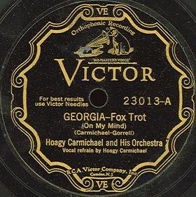 This is a photograph of a vintage Victor Records label from 1930. The label features the classic Victor design with ornate golden decorative scrollwork framing the text against a black background. At the top is the Victor company logo.

The record label shows:

Catalog number: 23013-A
Song title: "GEORGIA—Fox Trot" with "(On My Mind)" in parentheses
Composer credit: "(CARMICHAEL-GORRELL)"
Artist: "Hoagy Carmichael and His Orchestra"
Vocal credit: "Vocal Refrain by Hoagy Carmichael"

This is significant historical evidence showing that both Hoagy Carmichael and Stuart Gorrell were credited as co-writers from the original 1930 recording, contradicting the legend that Carmichael initially left Gorrell off the copyright and later voluntarily paid him royalties. The label clearly shows both names were credited from the beginning.

https://en.wikipedia.org/wiki/Georgia_on_My_Mind#/media/File:Hoagy-georgia-on-my-mind.jpg