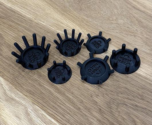 6 black 3D-printed circular objects with varying numbers of protruding spikes, displayed on a wooden surface.