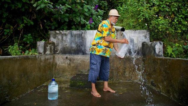 Un habitant remplit un récipient avec de l'eau provenant d'une source naturelle à Trois-Rivières en Guadeloupe, le 26 juillet 2018.