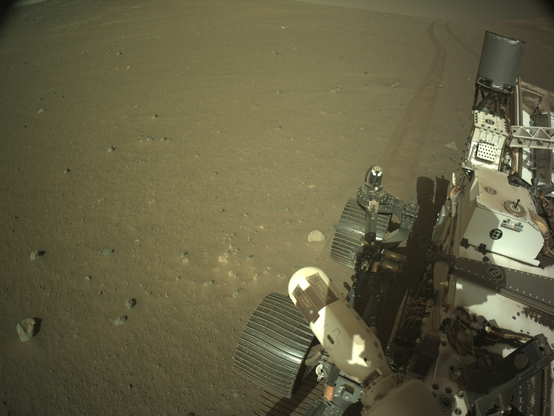 Image captured on the slopes of the rim of Jezero Crater, with the Mars rover Perseverancea in the foreground to the right, with rover tracks receding away in te distance.