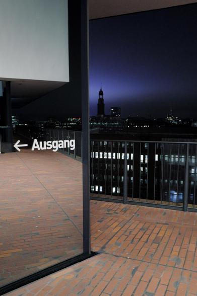 Blick von der Elphi auf den Michel bei Dämmerung, Hinweis „Ausgang“ auf verspiegelter Wand im Vordergrund