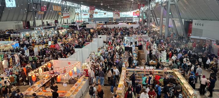 Bild von einem Empore aus aufgenommen mit Blick auf eine der vier Messehallen der ComicCon Stuttgart. Sehr viele Leute sind rund um verschiedene Verkaufsstände und Buden.