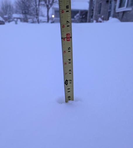A yellow tape measure in a pile of white snow, with the snow reaching the 10" mark. 